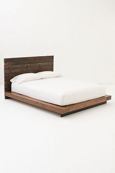 a bed with a wooden headboard and foot board on top of it, against a white wall