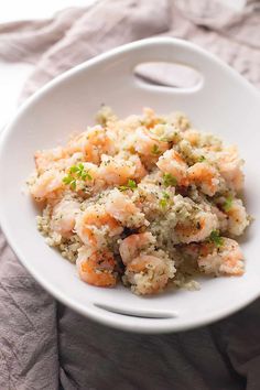 a white bowl filled with rice and shrimp on top of a bed of linens