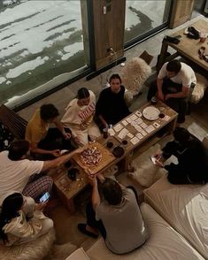 a group of people sitting around a table with pizzas on it in front of a window