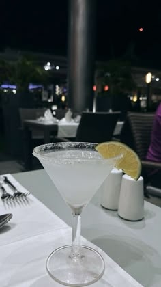 a white table topped with a martini glass filled with liquid and garnished with a lemon slice