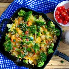 a casserole dish with broccoli, cheese and tomatoes on the side