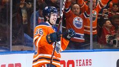 an orange jerseyed hockey player holding his stick in front of the ice and fans