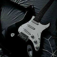 a black and white photo of an electric guitar on top of a bed with pillows