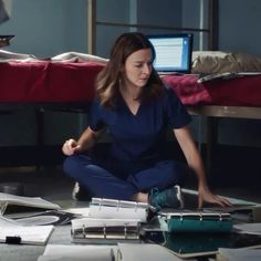 a woman in scrubs sitting on the floor surrounded by papers and laptop computer equipment