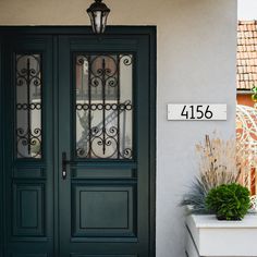 the front door to a house with a number plate on it and potted plants