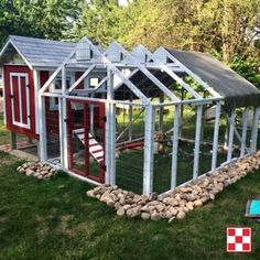 a chicken coop in the middle of a yard with rocks around it and a red house on top