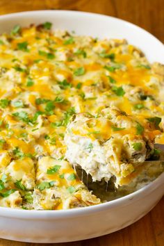 a casserole dish filled with chicken, cheese and green onions on a wooden table