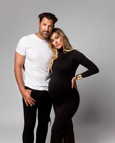 a pregnant couple posing for a photo in black pants and white t - shirt with their arms around each other