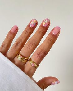 a woman's hand with pink and yellow flowers painted on it, holding two gold rings