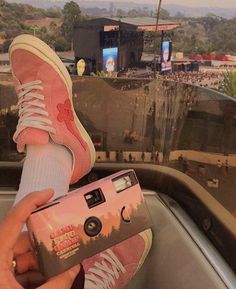 a person holding a camera in their hand and wearing pink sneakers on top of a car