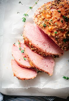 sliced ham on parchment paper with sprigs of thyling and seasoning next to it