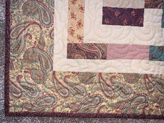 a close up of a quilted table runner with paisley designs on the border and center