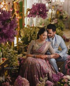 a man and woman sitting next to each other in front of purple flowers on display