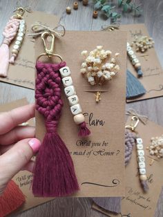 a hand holding a card with some tassels and beads attached to the back