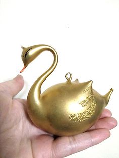 a gold swan ornament in the palm of someone's hand on a white background