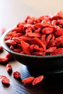 a bowl filled with red goji berries on top of a wooden table