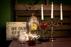 a table topped with candles and a clock next to a sign that says be our gift