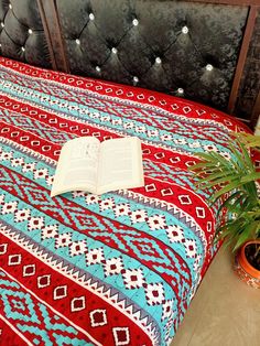 an open book sitting on top of a bed next to a potted green plant