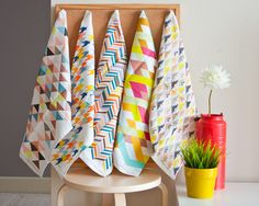 several colorful towels hanging on a wall next to a potted plant and yellow vase