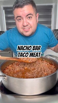 a man holding a wooden spoon in front of a large pot filled with taco meat