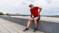 a man sitting on the edge of a concrete wall next to a body of water