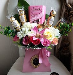 a pink box filled with assorted flowers and chocolates on top of a white chair