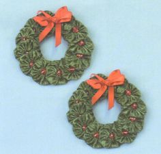 two green wreaths with red bows are on a blue background and one has an orange bow