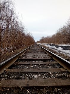 an old train track with snow on the ground and bare trees in the backround