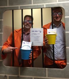 two men in jail cell holding up signs and buckets with papers taped to them