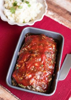 meatloaf with sauce and mashed potatoes on a red place mat next to a bowl of rice