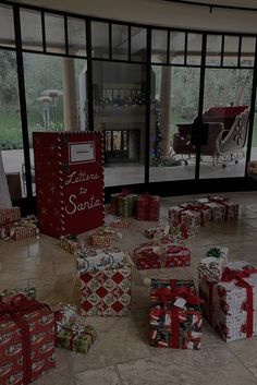 many wrapped presents sit on the floor in front of large windows