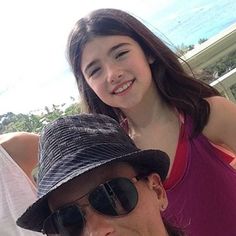 a man and woman sitting next to each other in front of a building with the ocean behind them