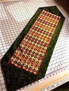 a quilted table runner sitting on top of a cutting board next to a ruler