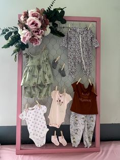 a pink frame with baby clothes and flowers on the top, next to a bouquet of flowers