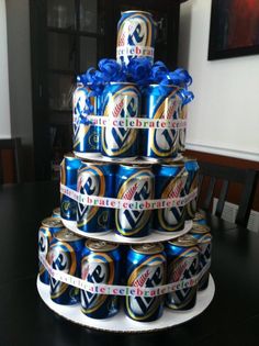 a tiered cake made out of beer cans with blue ribbon around the top and bottom