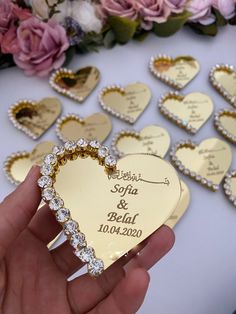 a person holding a heart shaped brooch with wedding date written on it and flowers in the background