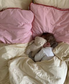 a baby sleeping in bed with a teddy bear