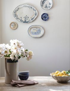 white flowers in a blue and white vase next to plates on the wall behind it