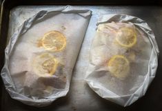 two uncooked fish with lemon slices on top of parchment paper in a pan