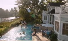 an outdoor swimming pool with people in it and sun shining on the house's roof