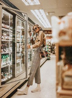 a woman standing in front of a glass case filled with drinks and sodas at a grocery store