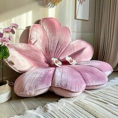 a large pink flower sitting on top of a wooden floor next to a potted plant