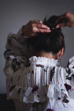 a woman with her hair in a bun is wearing a white blouse and has flowers on it