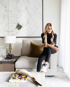 a woman sitting on top of a couch in a living room next to a painting