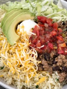 a white bowl filled with rice, meat and veggies next to an avocado