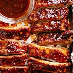 ribs covered in bbq sauce and sitting on tin foil next to a bowl of ketchup