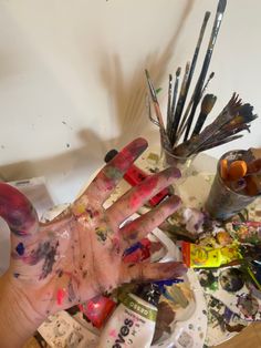 a person's hand covered in paint and other art supplies on top of a table