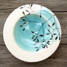 a white and blue bowl with black leaves on it sitting on a wooden table top