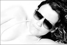 a woman wearing sunglasses laying on top of a white bed next to a black and white photo