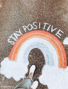 someone standing in front of a chalk drawing that says stay positive with a rainbow and clouds